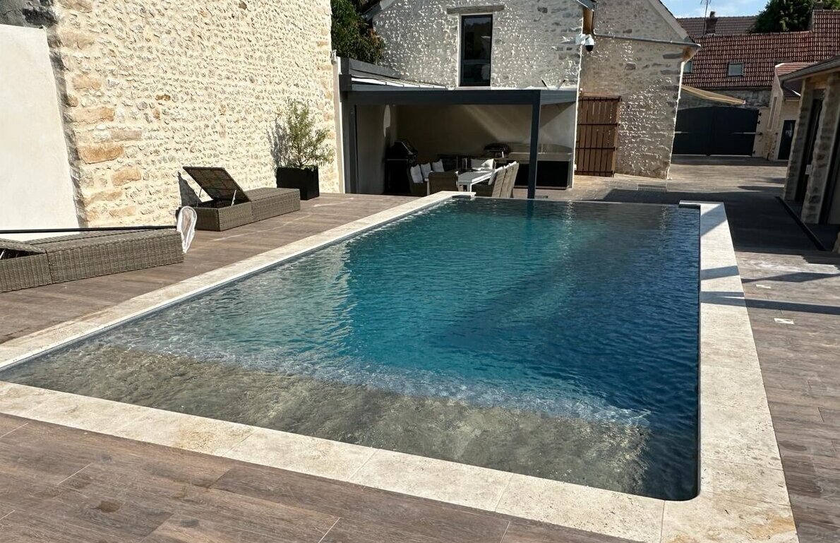Piscine en béton armé avec terrasse au pied d'une maison en pierre